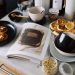 High angle of cookbook and cooked fritters on plates placed on table near utensils and ingredients in cozy kitchen at home